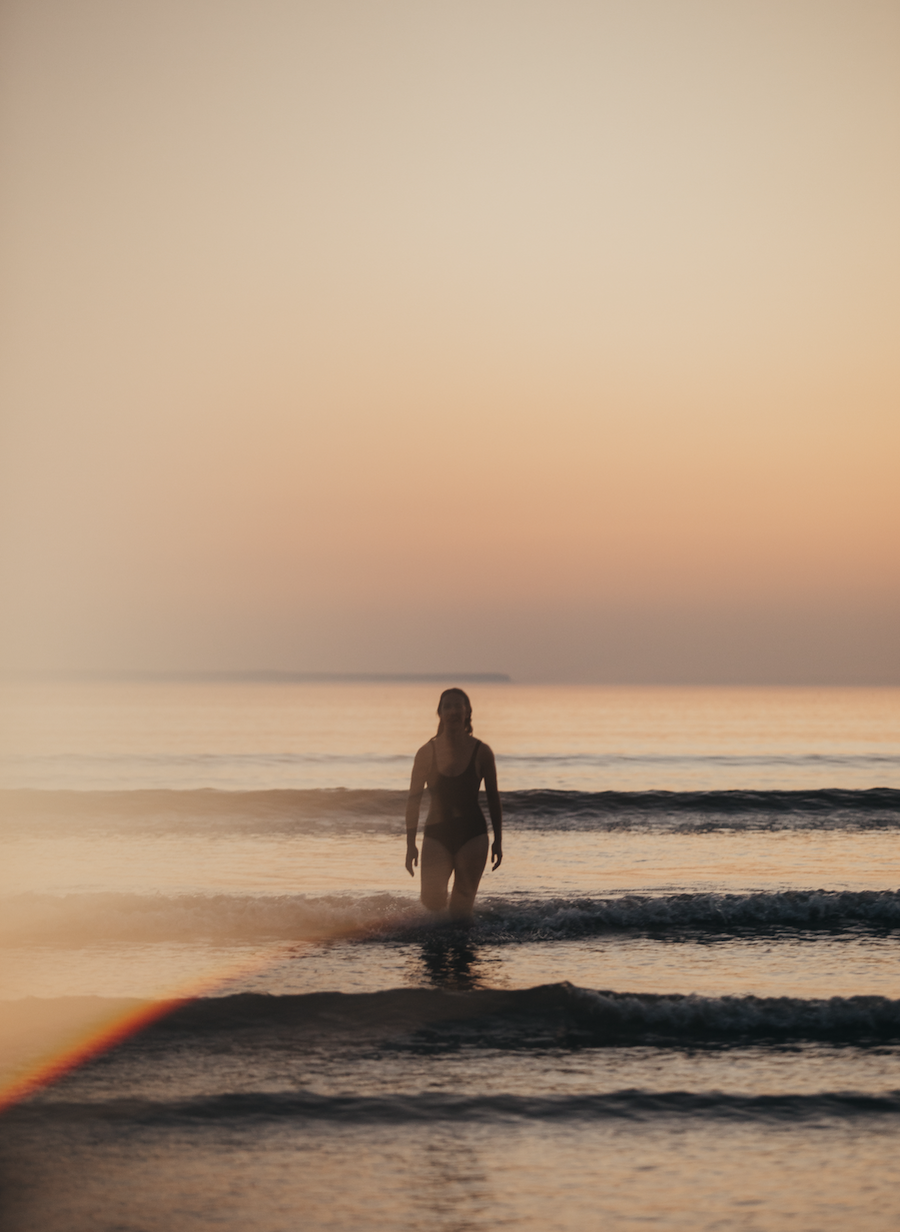 Krissie, business mentor out in the sea with black swimsuit on with beautiful sunset behind her.